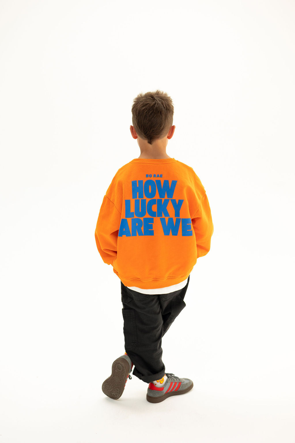 BO RAE How Lucky Are We oversized kids jumper in orange, back view featuring large blue graphic print.