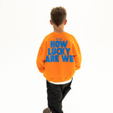 BO RAE How Lucky Are We oversized kids jumper in orange, back view featuring large blue graphic print.