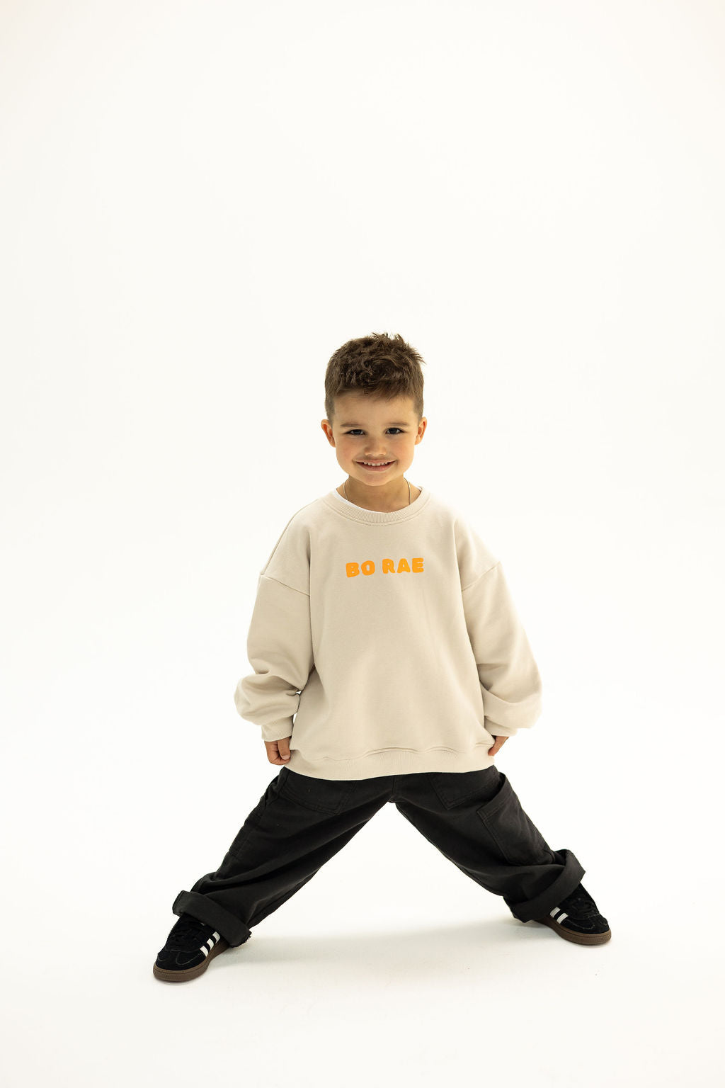 BO RAE Front view of BO RAE How Lucky Are We oversized kids jumper in Beige with orange chest logo