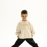 BO RAE Front view of BO RAE How Lucky Are We oversized kids jumper in Beige with orange chest logo