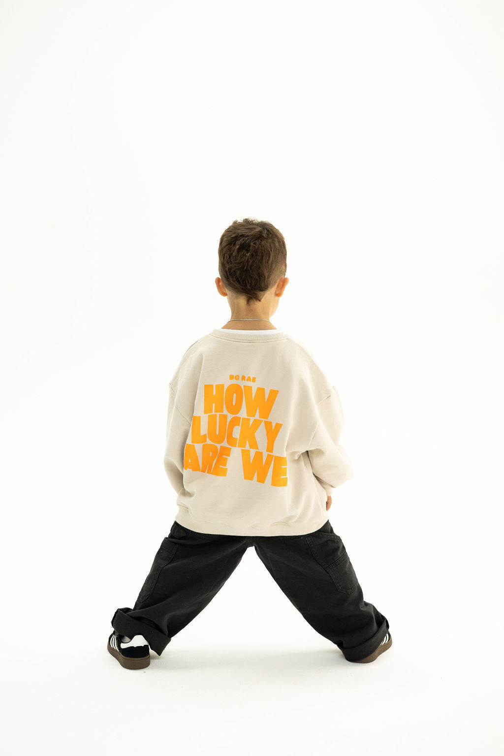 Back view of BO RAE How Lucky Are We oversized kids jumper in Beige featuring large orange graphic print.