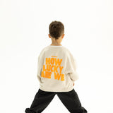 Back view of BO RAE How Lucky Are We oversized kids jumper in Beige featuring large orange graphic print.