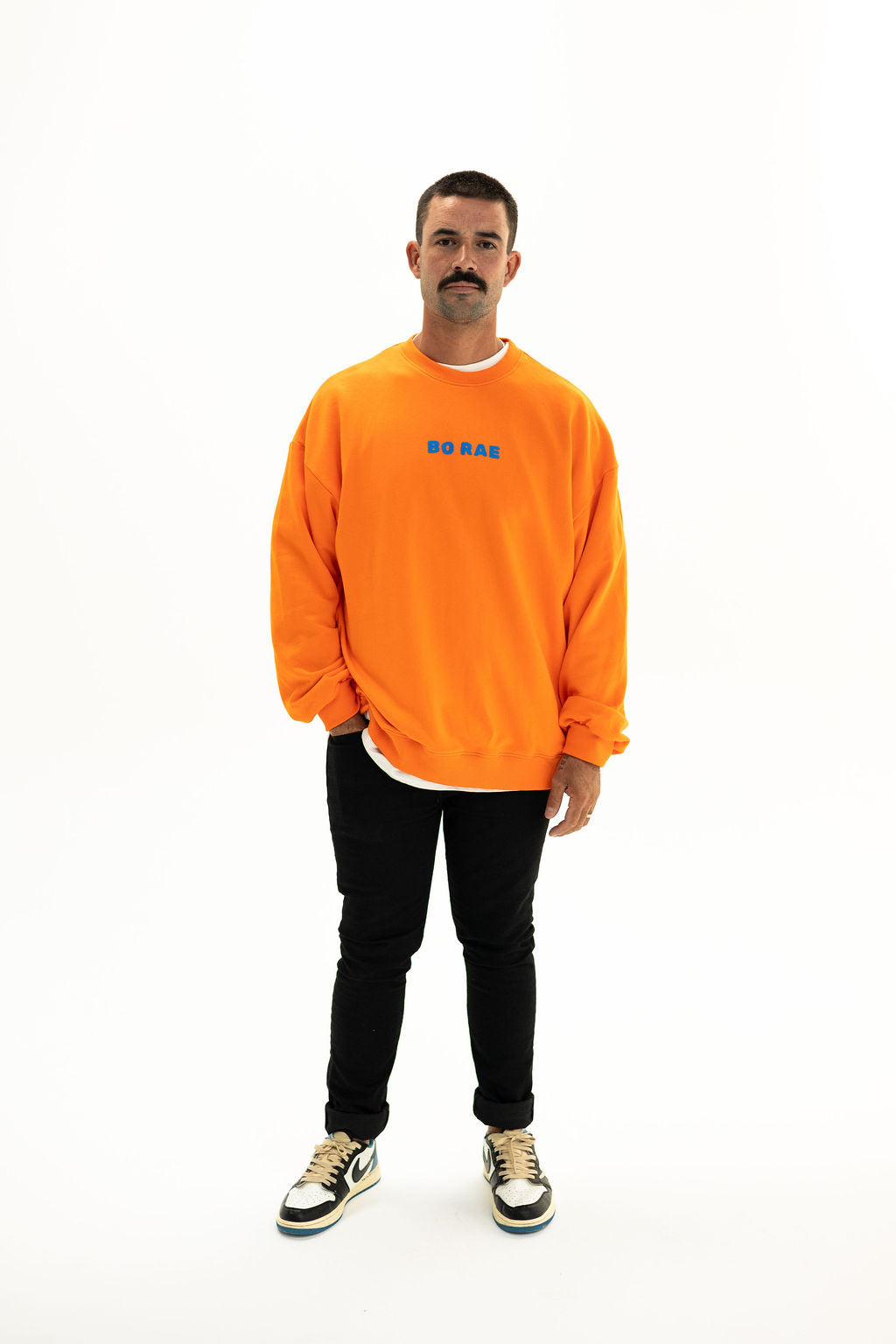 Model wearing BO RAE How Lucky Are We oversized unisex adult jumper in orange with blue chest logo