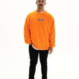 Model wearing BO RAE How Lucky Are We oversized unisex adult jumper in orange with blue chest logo