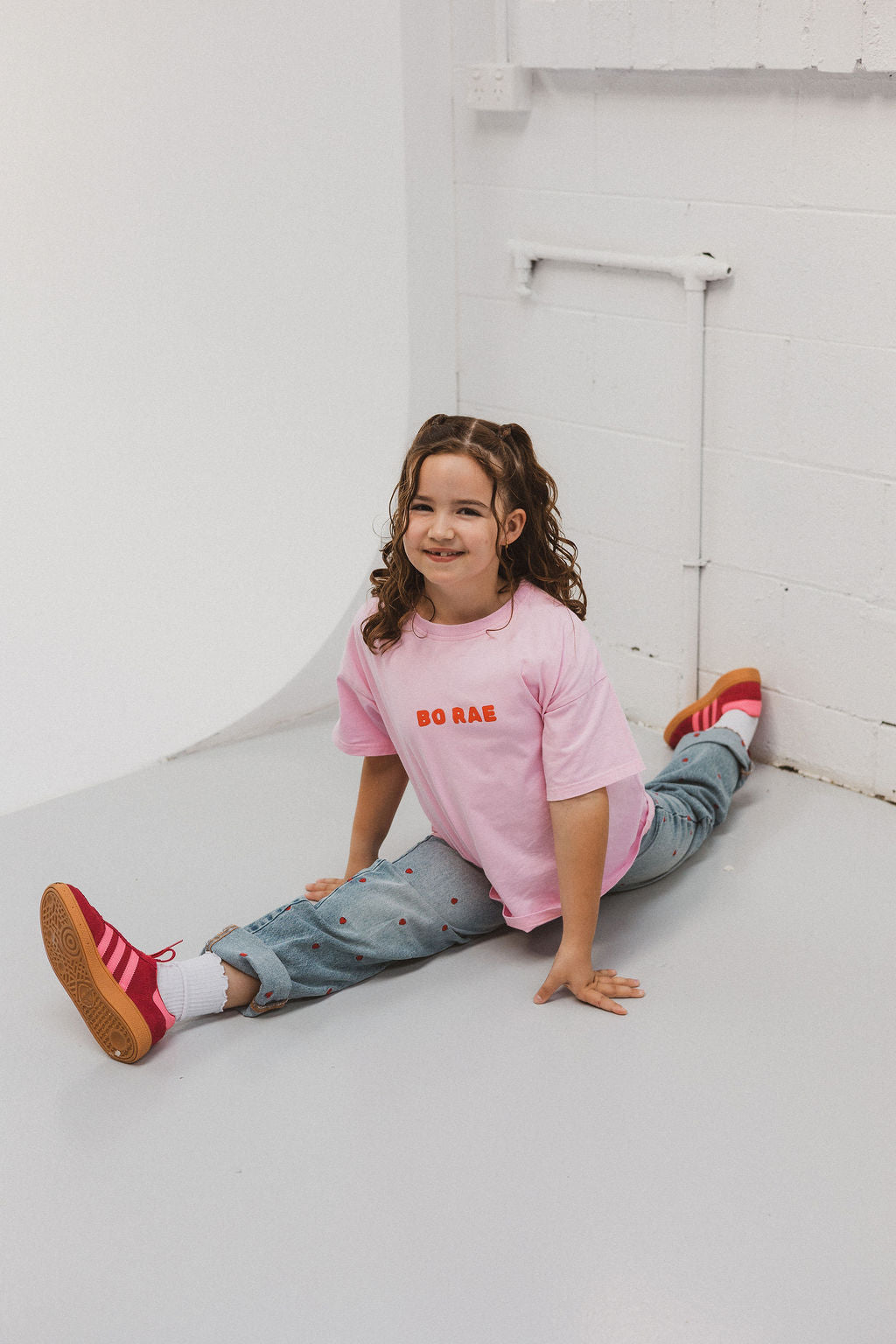 Child wearing BO RAE How Lucky Are We oversized kids T-shirt in pink while sitting.