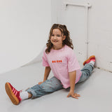 Child wearing BO RAE How Lucky Are We oversized kids T-shirt in pink while sitting.