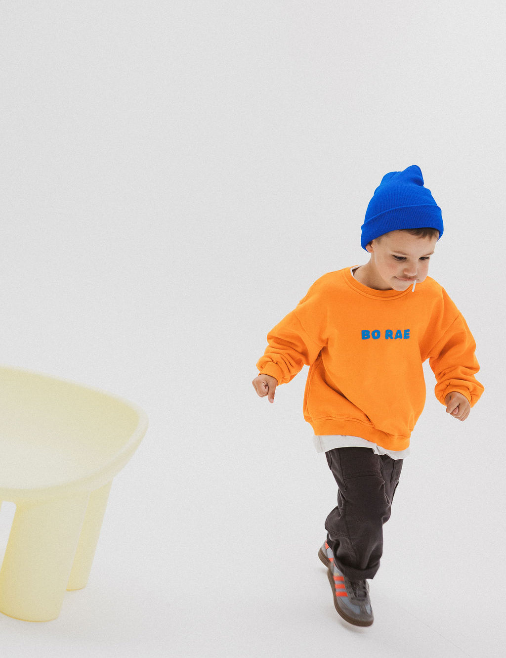 Child wearing BO RAE How Lucky Are We oversized kids jumper in orange while running.