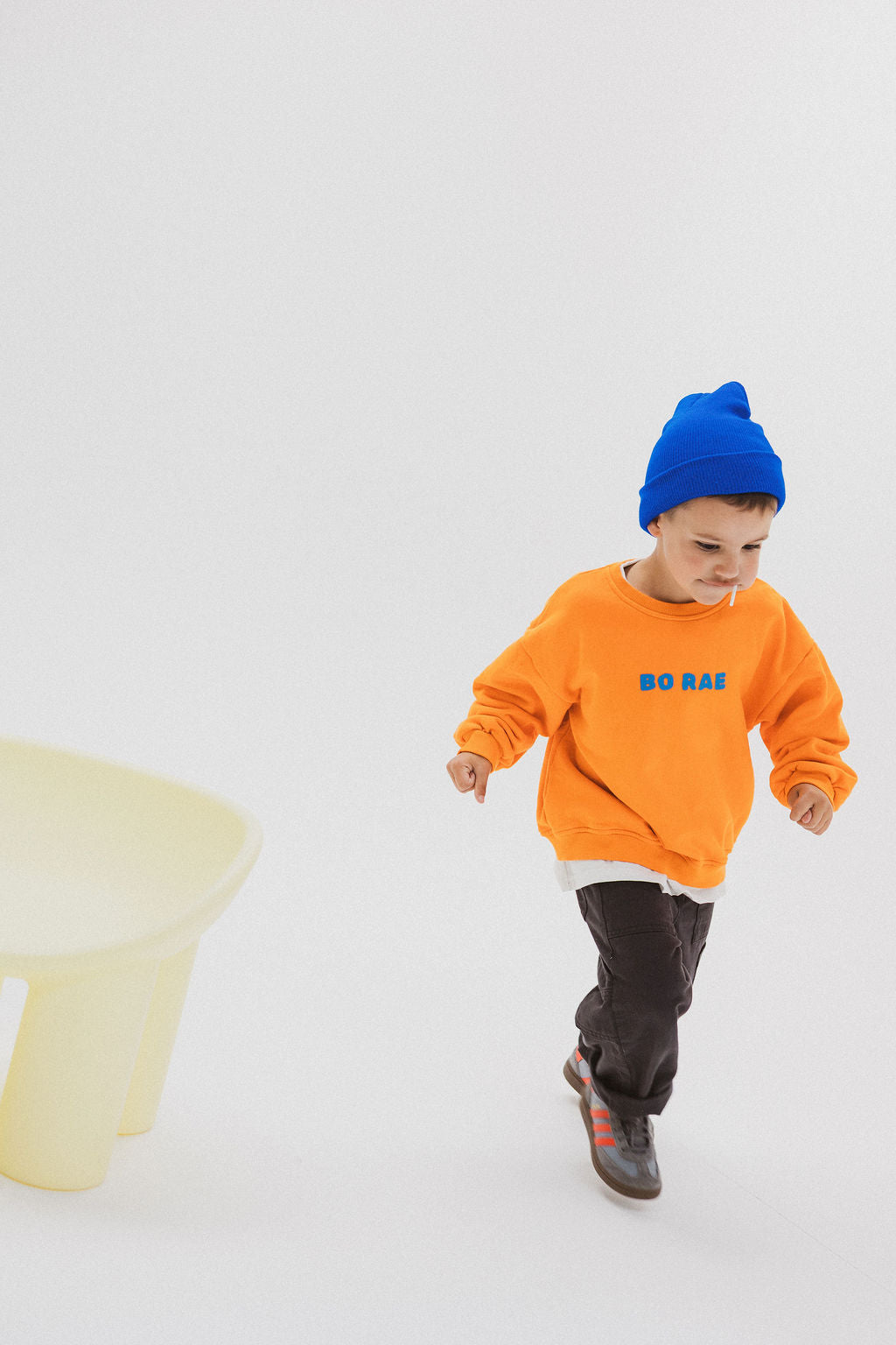 Child wearing BO RAE How Lucky Are We oversized kids jumper in orange while running.