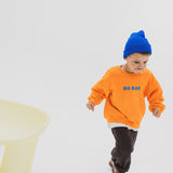 Child wearing BO RAE How Lucky Are We oversized kids jumper in orange while running.