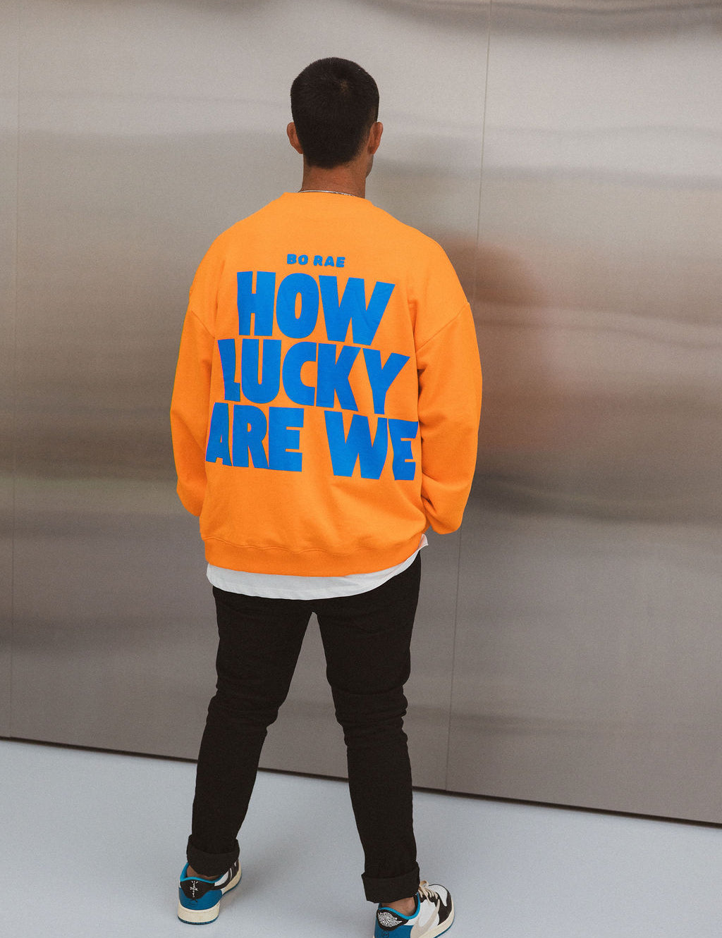Model wearing BO RAE How Lucky Are We oversized orange adult jumper with large blue back graphic