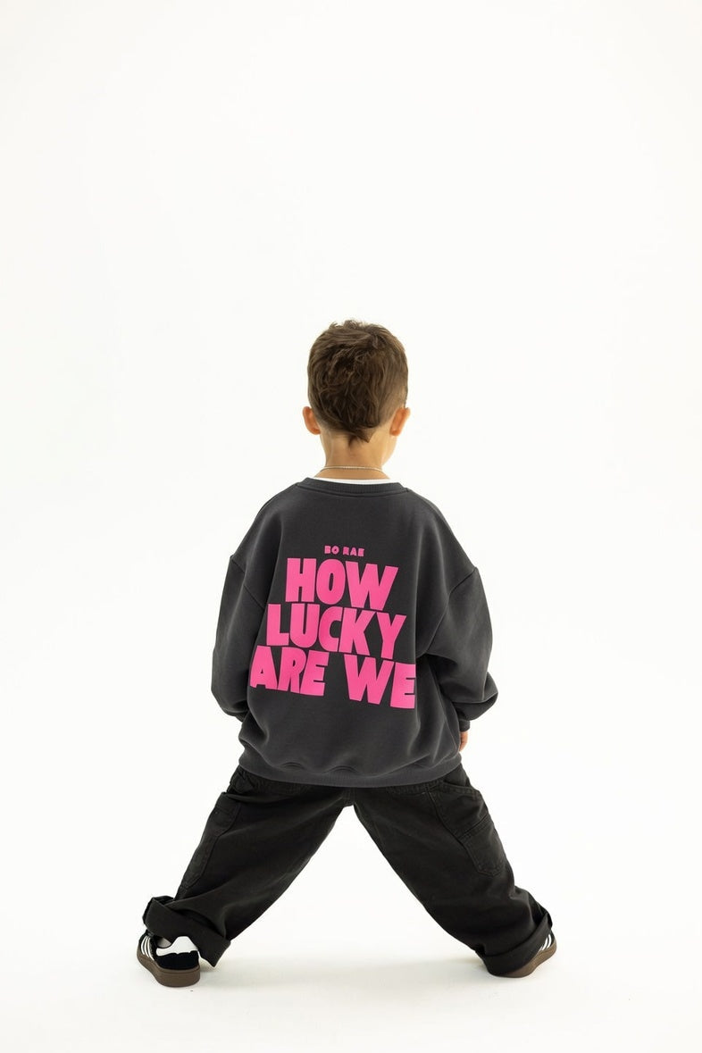 Back view of BO RAE How Lucky Are We oversized kids jumper in Khaki Slate Grey featuring large pink graphic print.