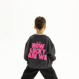 Back view of BO RAE How Lucky Are We oversized kids jumper in Khaki Slate Grey featuring large pink graphic print.