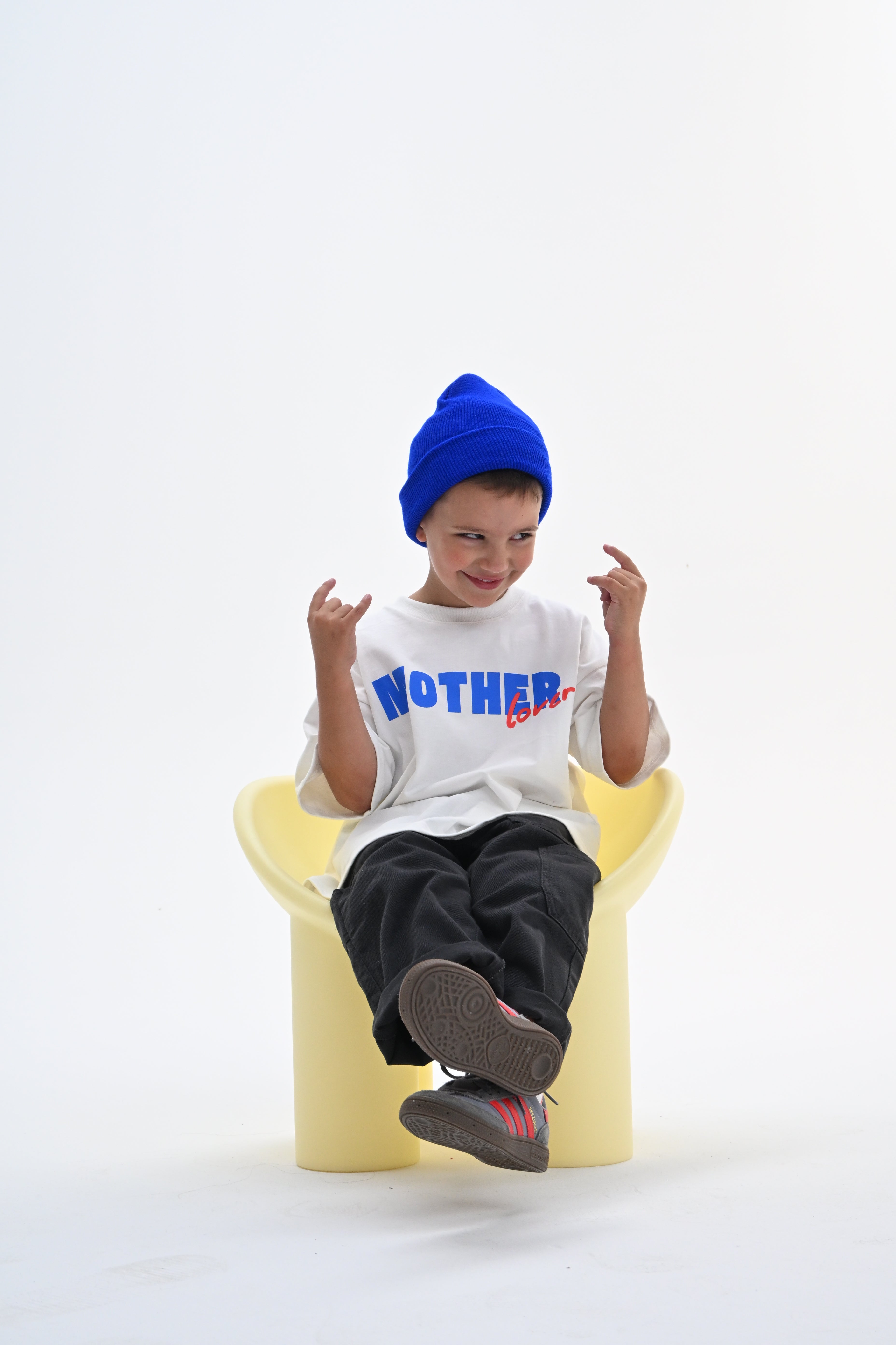 BO RAE How Lucky Are We oversized kids T-shirt in white, child sitting on chair wearing blue beanie.